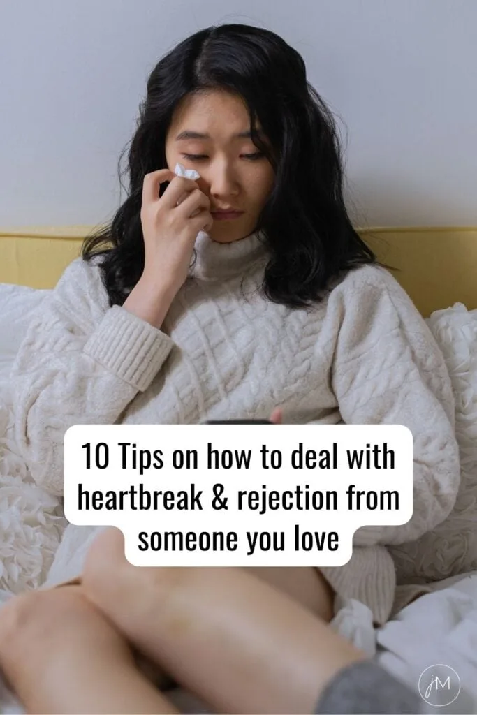 asian woman sitting on bed and crying into a tissue