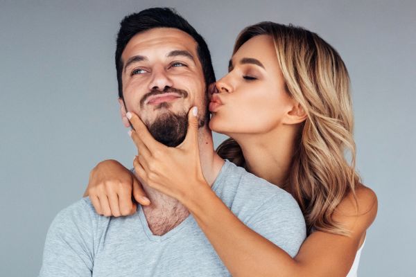 young woman kissing young man on his cheek while he smirks