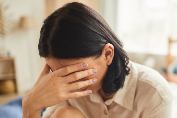 young woman with dark hair, holing hand in front of her face