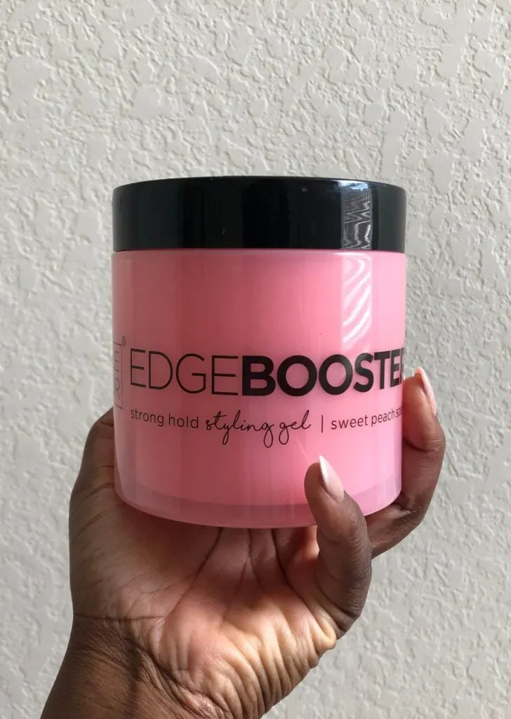 Manicured black hand holding pink Style Factor Edge Booster Gel in front of white wall