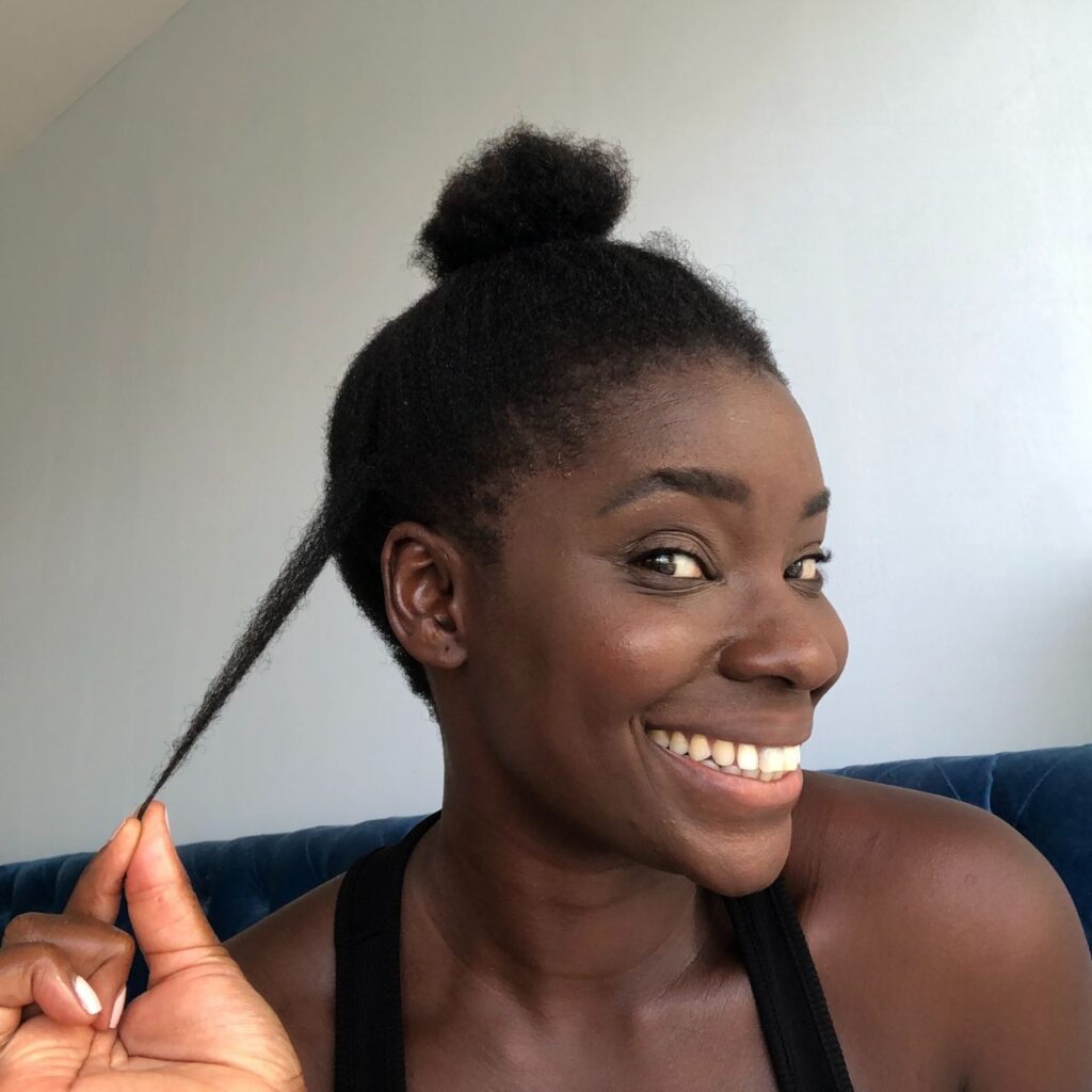 black woman holding a hair strand of her natural 4c hair while laughing into the camera