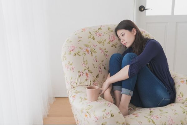 sad young woman couped up on a sofa with a cup of tea