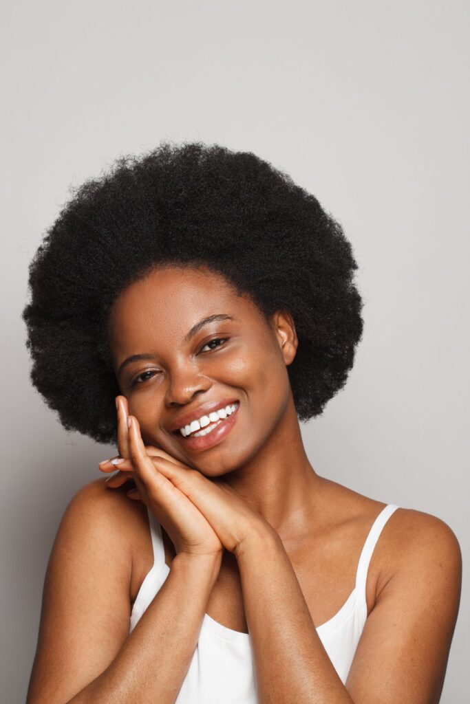 black woman with an afro smiling into the camera in front of grey background