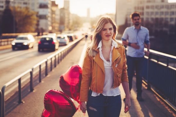 young woman walking away from man while holding heart balloons