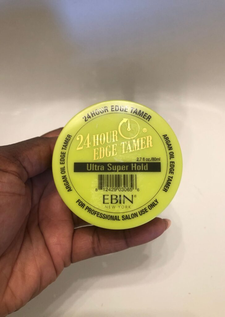 black hand holding tub of EBIN New York 24-hour Edge Tamer in front of the sink