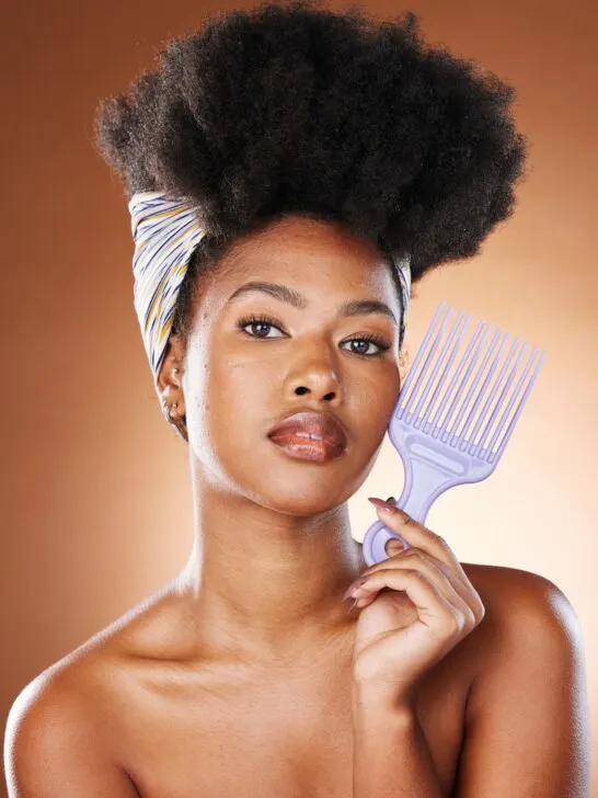 young black woman with beautiful afro hair holding a comb to her face in front of a brown background