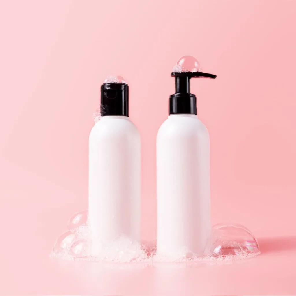 two white hair bottles in front of a pink background