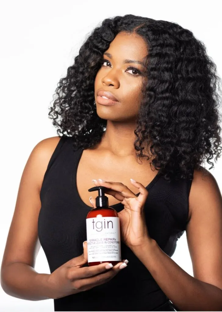 Black woman holding tgin Leave In Conditioner