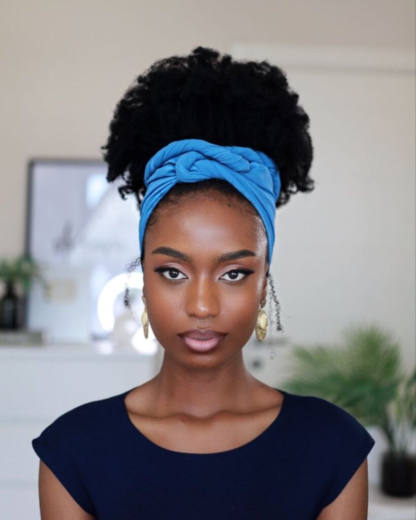 Young woman with a blue headscarf around her high puff looking into the camera