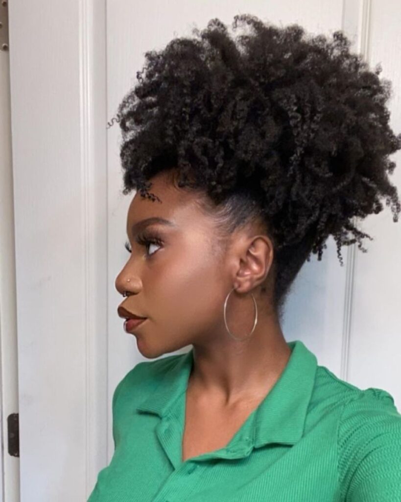 Black woman with a green blouse showing off her curly afro puff