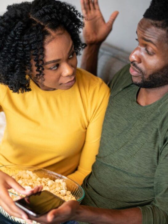 black couple sitting on the couch debating and eating popcorn