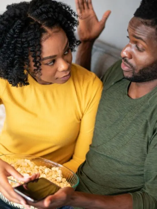 black couple sitting on the couch debating and eating popcorn
