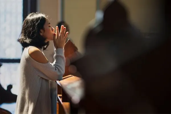 young woman in church with arms lifted in prayer pose