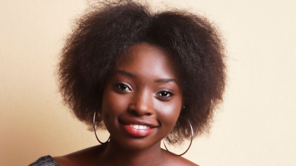 young black woman smiling into the camera in front of a cream background