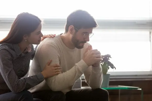 young couple looking sad while woman is consoling the man