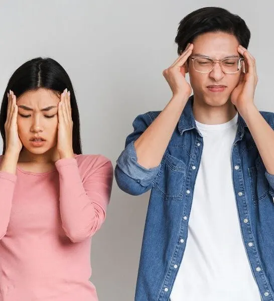 young asian couple standing in front of grey background shaking their heads