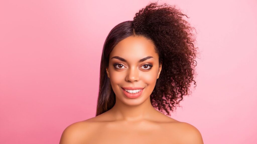 young woman smiling into camera in front of pink background