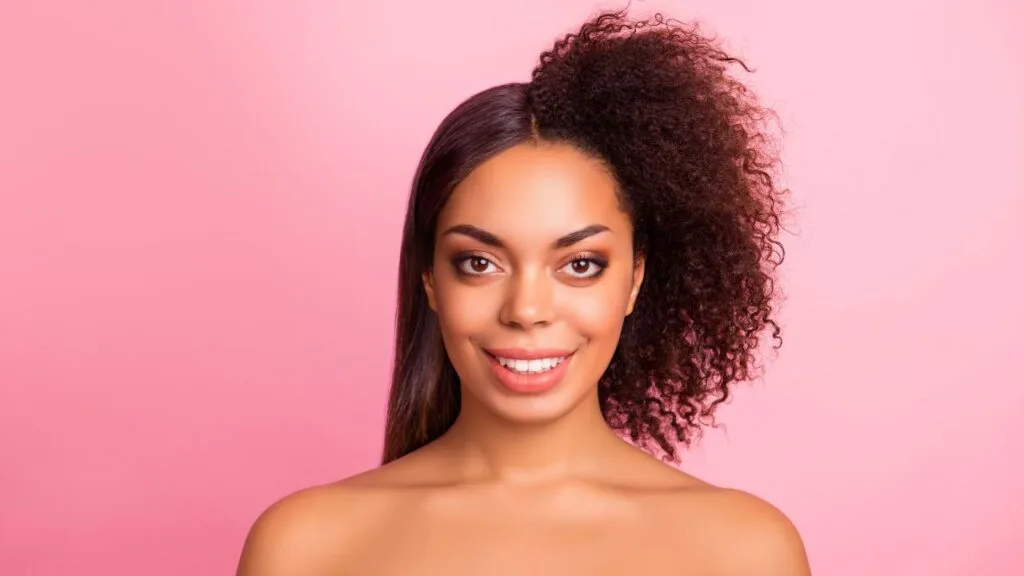 young woman smiling into camera in front of pink background