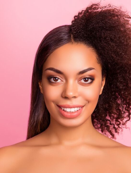 young woman smiling into camera in front of pink background