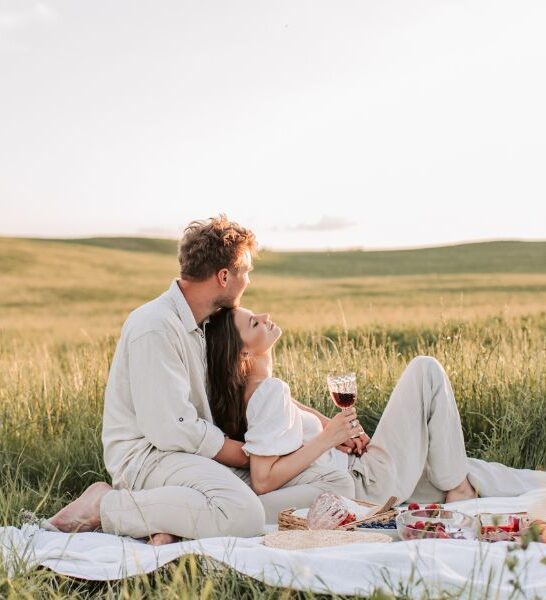 young couple dressed in white sitting on a blanket in a field