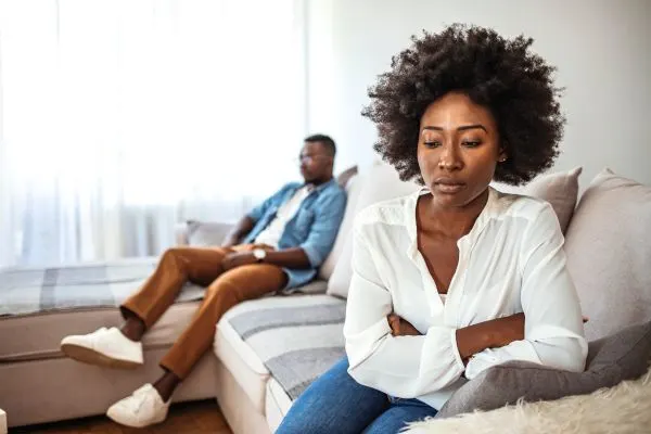young black couple sitting on opposite side of the couch while looking angry